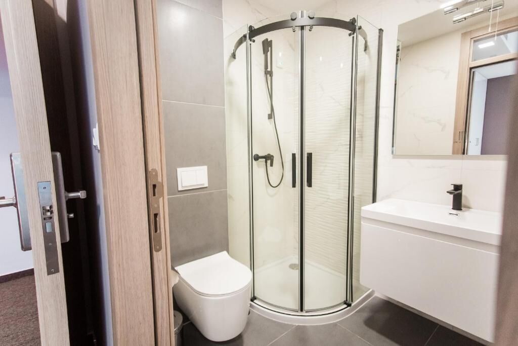 Un baño moderno con ducha de mampara de vidrio, inodoro blanco y tocador blanco con espejo.