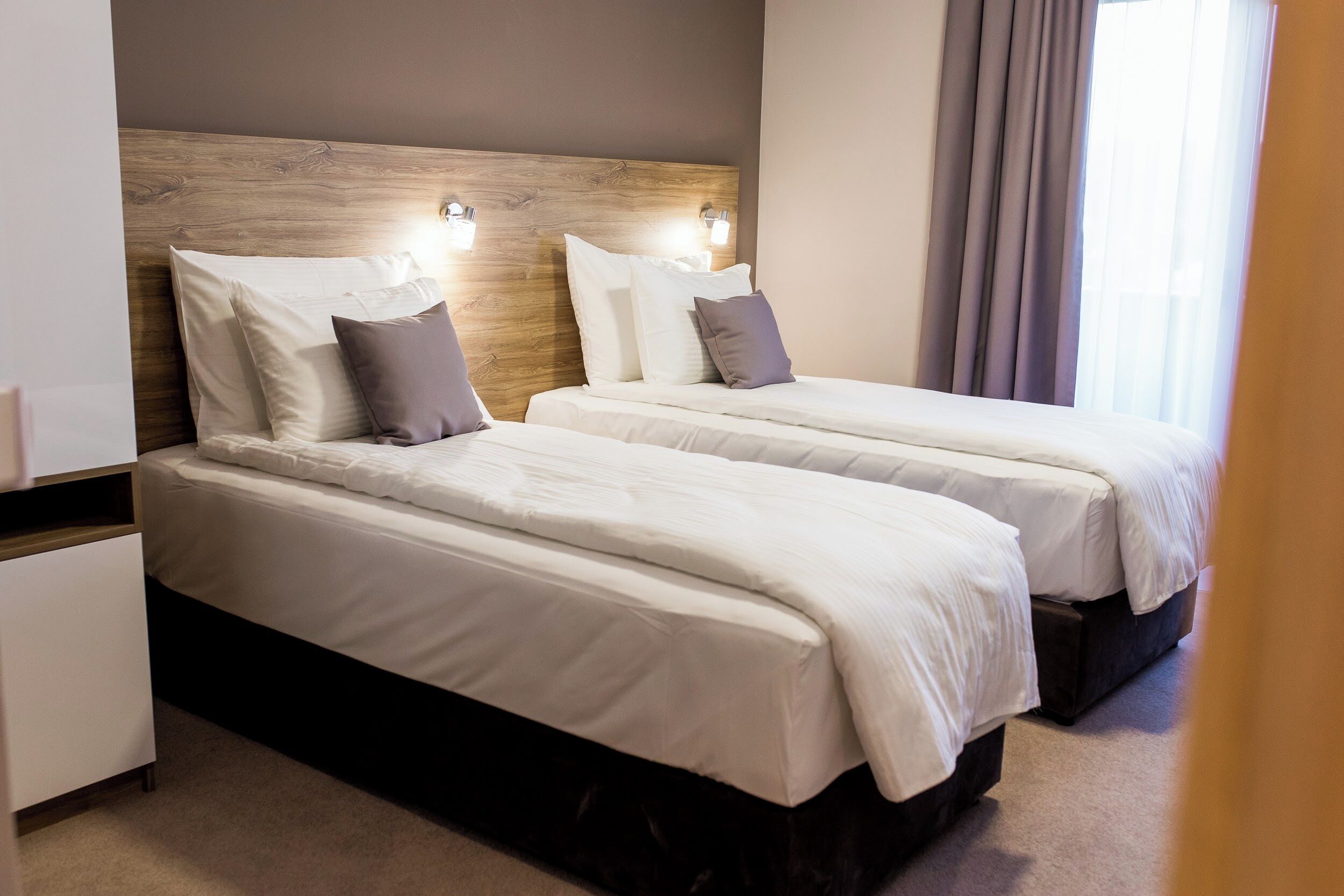 A hotel room with two beds, a wooden headboard, and a nightstand.