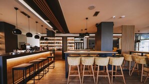 Uma área de bar moderna com piso de madeira, banquetas pretas e luminárias pendentes.
