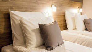 Quarto de hotel com cabeceira de madeira, duas camas com roupa de cama branca e luminárias fixadas na parede.