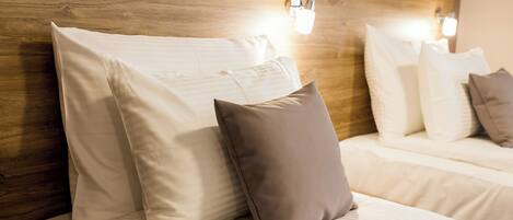 Una habitación de hotel con cabecera de madera, dos camas con ropa blanca y lámparas fijadas a la pared.