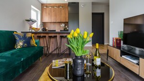 A modern living room with a green sofa, a coffee table with a vase of yellow flowers, a magazine, and a bottle of wine. - Lumina deluxe 3-room apartment (Lodz)