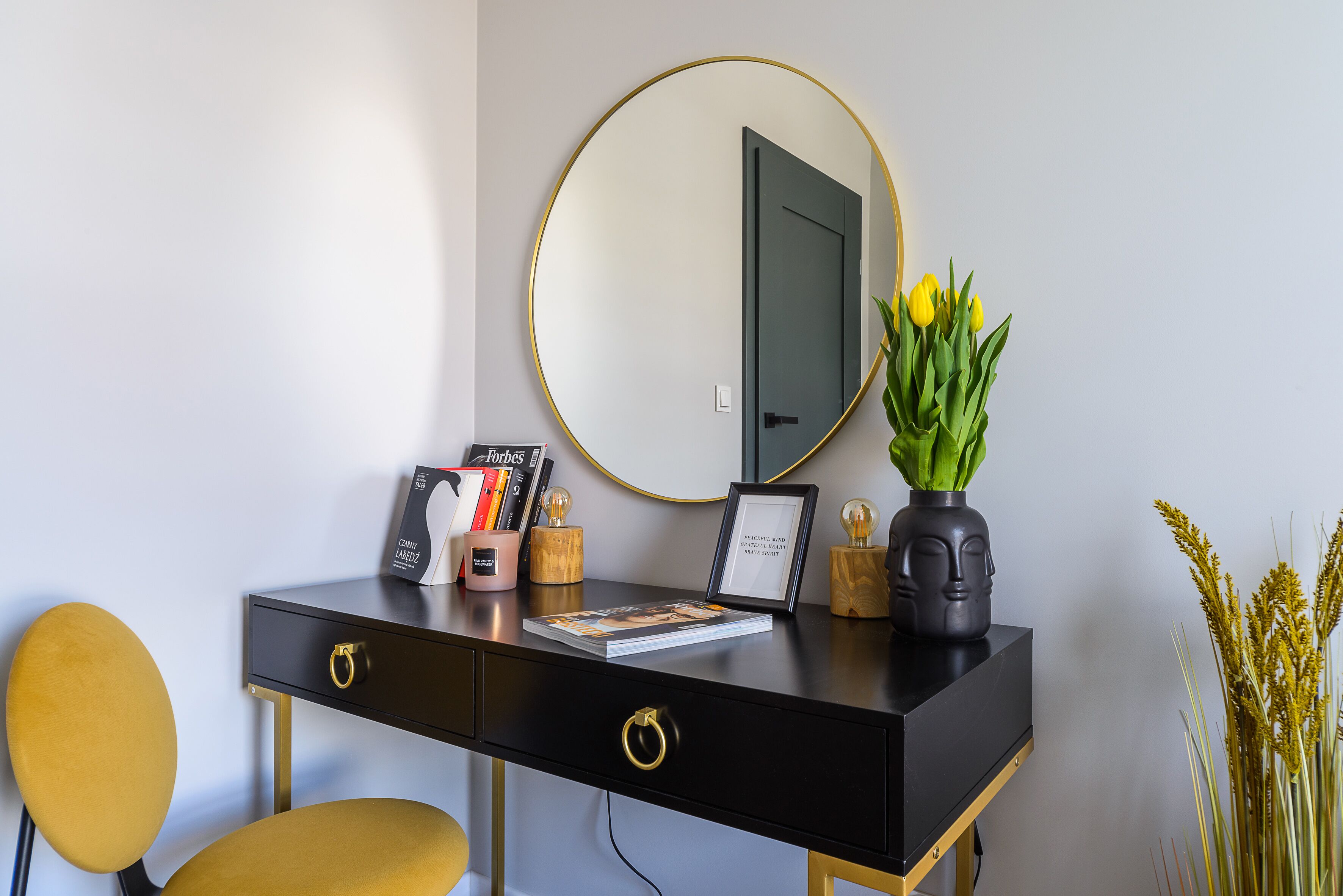 A modern desk with a black finish, gold accents, and a round mirror above it.