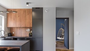 A modern kitchen with wooden cabinets, a stainless steel refrigerator, and a bar area with stools. - Lumina deluxe 3-room apartment (Lodz)