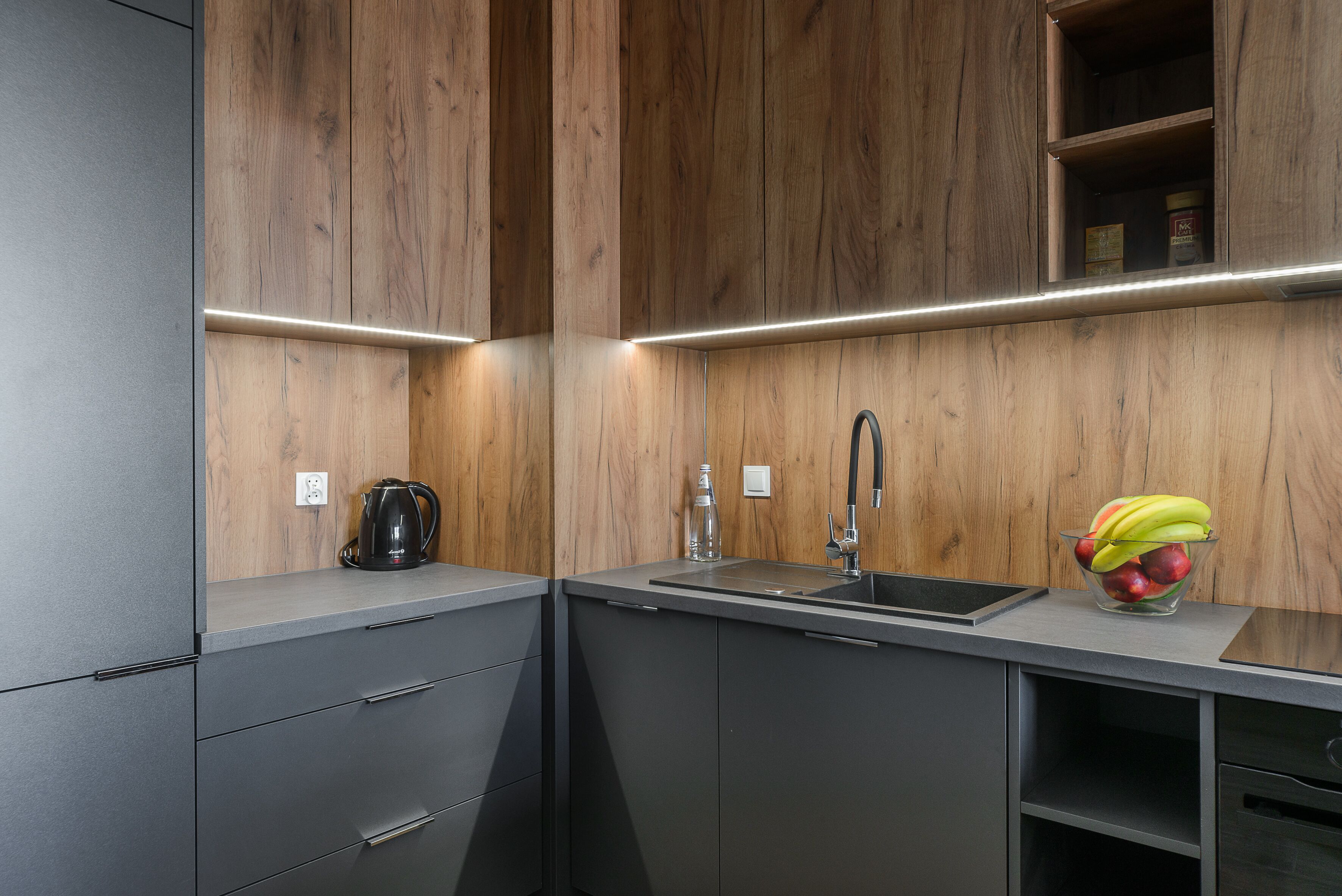 A modern kitchen with wooden cabinetry, a stainless steel sink, and a fruit bowl on the countertop.