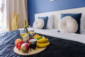 A bed with a dark blue bedspread, white pillows, and a wooden tray with fruits and a bottle of wine.