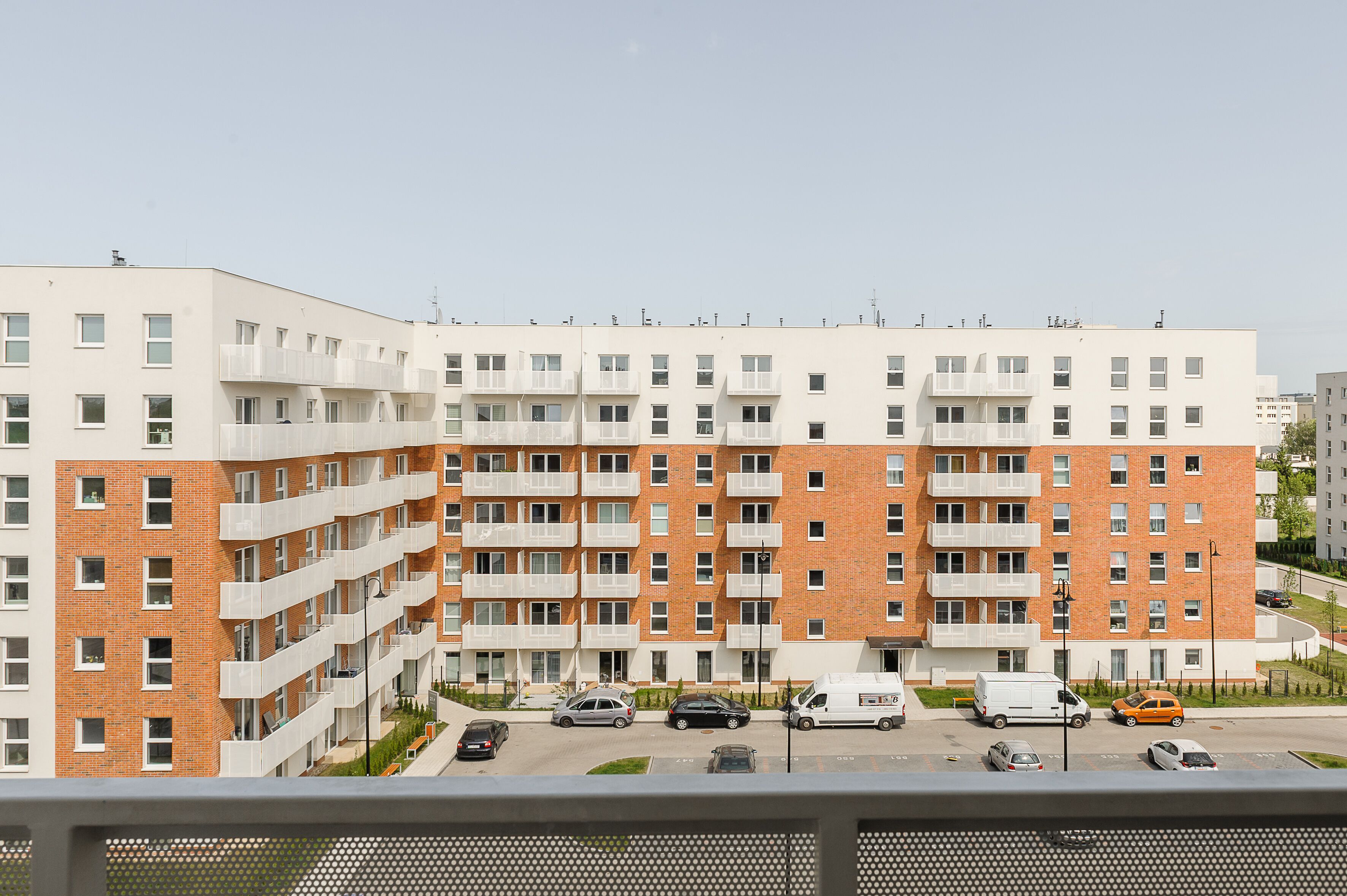 Un immeuble résidentiel à plusieurs étages doté de balcons, un espace de stationnement avec plusieurs voitures et un ciel dégagé.