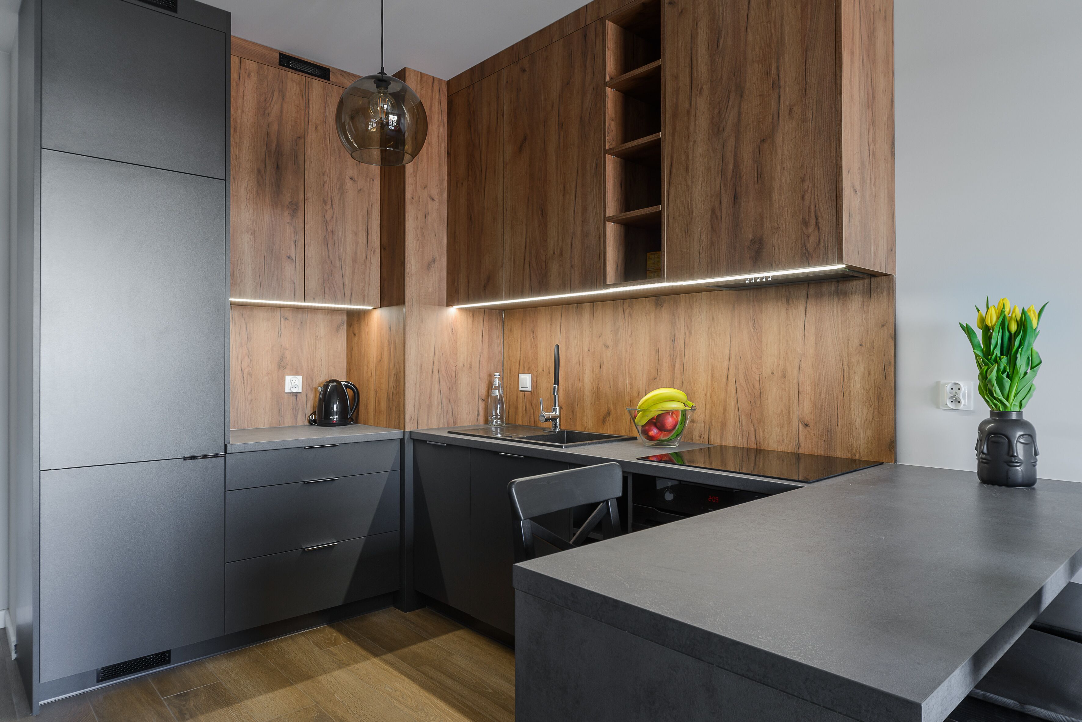 A modern kitchen with wooden cabinets, a black countertop, and a built-in dishwasher.