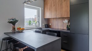 A modern kitchen with a large island, wooden cabinets, and a view of the city. - Lumina deluxe 3-room apartment (Lodz)