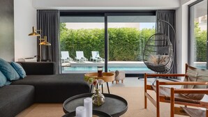 A modern living room with a sofa, coffee table, and hanging chair, overlooking a pool and lush greenery. - Villa Marli (Nin)