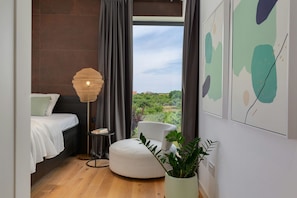 Quarto moderno com cama, mesa de cabeceira, luminária e vista para área verde.