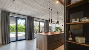 A modern kitchen with a large island, pendant lighting, and a view of a swimming pool. - Villa Marli (Nin)