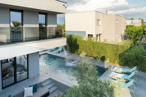 Uma área de piscina moderna ao ar livre, com guarda-corpo de vidro, espreguiçadeiras e uma escadaria que dá para uma varanda.