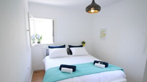 Een keurig opgemaakt slaapkamer met een bed, kussens en een hanglamp.