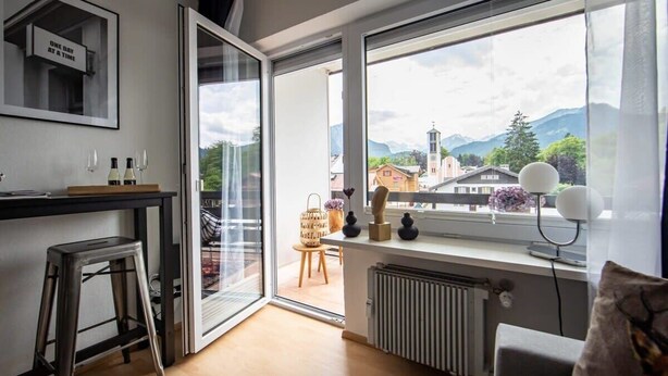 Een moderne keuken met een groot raam, een kruk en uitzicht op een stad en bergen.