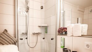 Een moderne badkamer met een douche met glazen wand, een witte wastafel en een spiegel erboven.