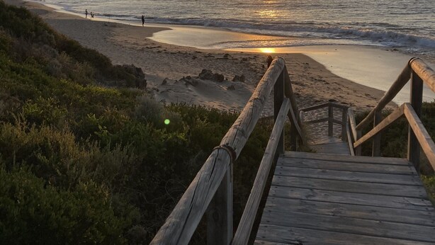 Una passerella di legno che conduce a una spiaggia, con il sole al tramonto sullo sfondo.