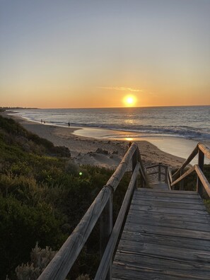 A wooden boardwalk leading to a beach with the sun setting in the background. - Modern Family Beach House 200m from the coast.  (Falcon)
