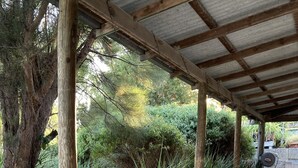 Un'area esterna coperta con tavoli da picnic, una panchina in cemento e un barbecue.