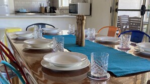 Zona pranzo con un tavolo lungo apparecchiato per un pasto, sedie e una cucina sullo sfondo.