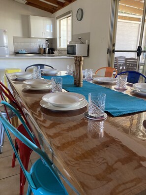 Een eethoek met een lange tafel gedekt voor een maaltijd, stoelen en een keuken op de achtergrond.
