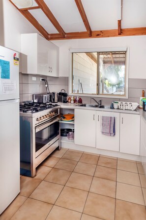 Een keuken met witte kastjes, een fornuis, een spoelbak en een raam boven de spoelbak.