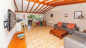 Un'ampia zona living con soffitto in legno, un divano grigio, un tavolino in legno e un'area pranzo con sedie colorate.