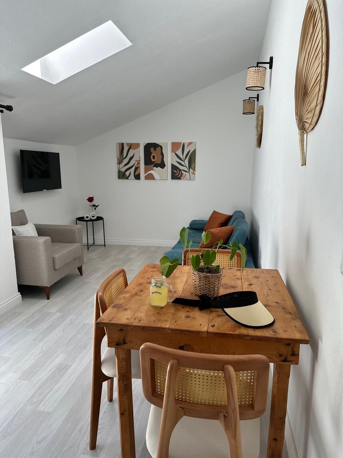 Un salon moderne avec une table à manger en bois, des chaises en osier, un canapé et un téléviseur fixé au mur.
