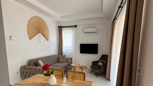 A modern living room with a wooden dining table, a sofa, and a TV mounted on the wall. - Likya Apart Kaş (Kas)