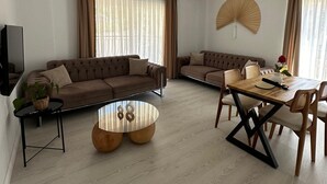 A modern living room with a sectional sofa, a round coffee table, and a dining area with a wooden table and chairs. - Likya Apart Kaş (Kas)