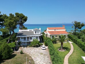 A coastal property with a stone driveway, two main buildings, and a view of the sea.