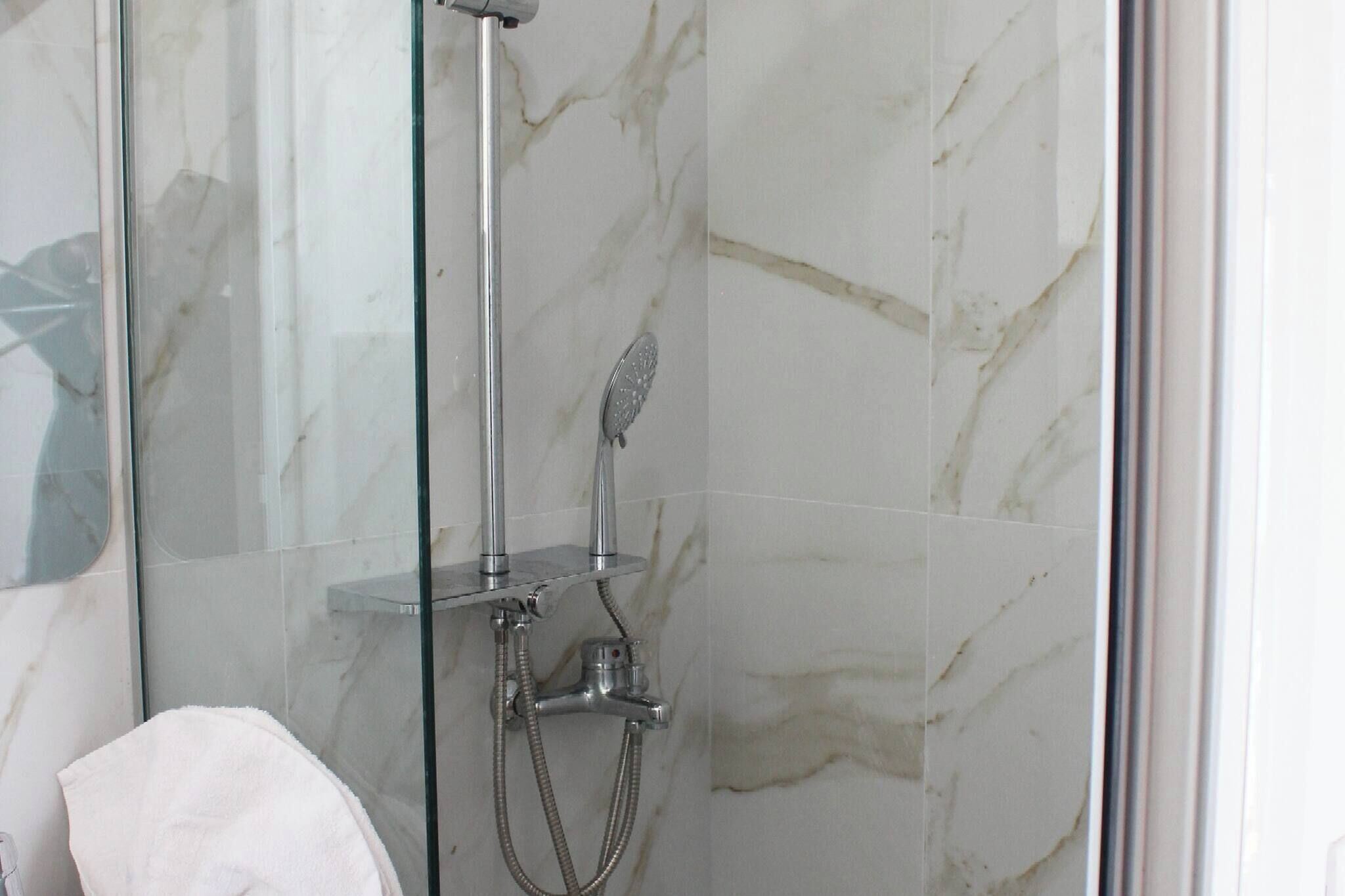 A glass-enclosed shower with a handheld showerhead and a wall-mounted faucet.