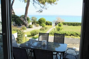 A table with chairs and a glass jar on a balcony overlooking a garden and the sea.