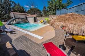 Une piscine dotée d’un toit de chaume et de chaises longues.
