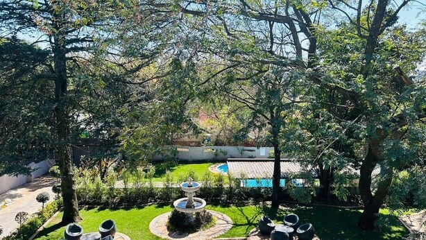 Un jardin bien entretenu, agrémenté d’une fontaine, de coins salon et d’une piscine en arrière-plan.