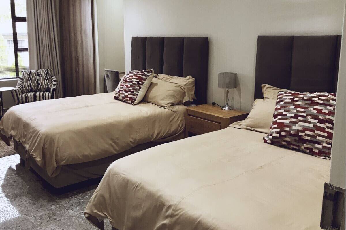 A hotel room with two beds, a chair, a nightstand, and a lamp.