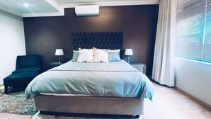 Une chambre moderne avec un grand lit, deux tables de chevet, une chaise et une fenêtre avec des stores.
