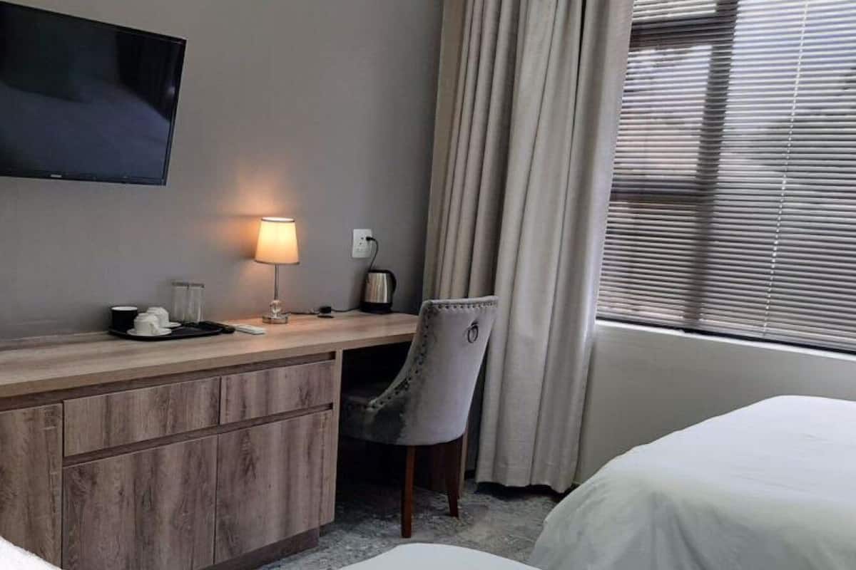 A hotel room with a wooden desk, a television mounted on the wall, a lamp, a chair, and a bed.