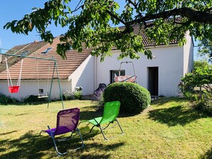 Ein weißes Haus mit rotem Ziegeldach, einer Schaukel und zwei Stühlen im Garten.
