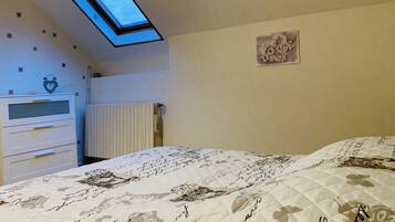 A bedroom with a skylight, a bed with floral bedding, a dresser, and a wall decoration.