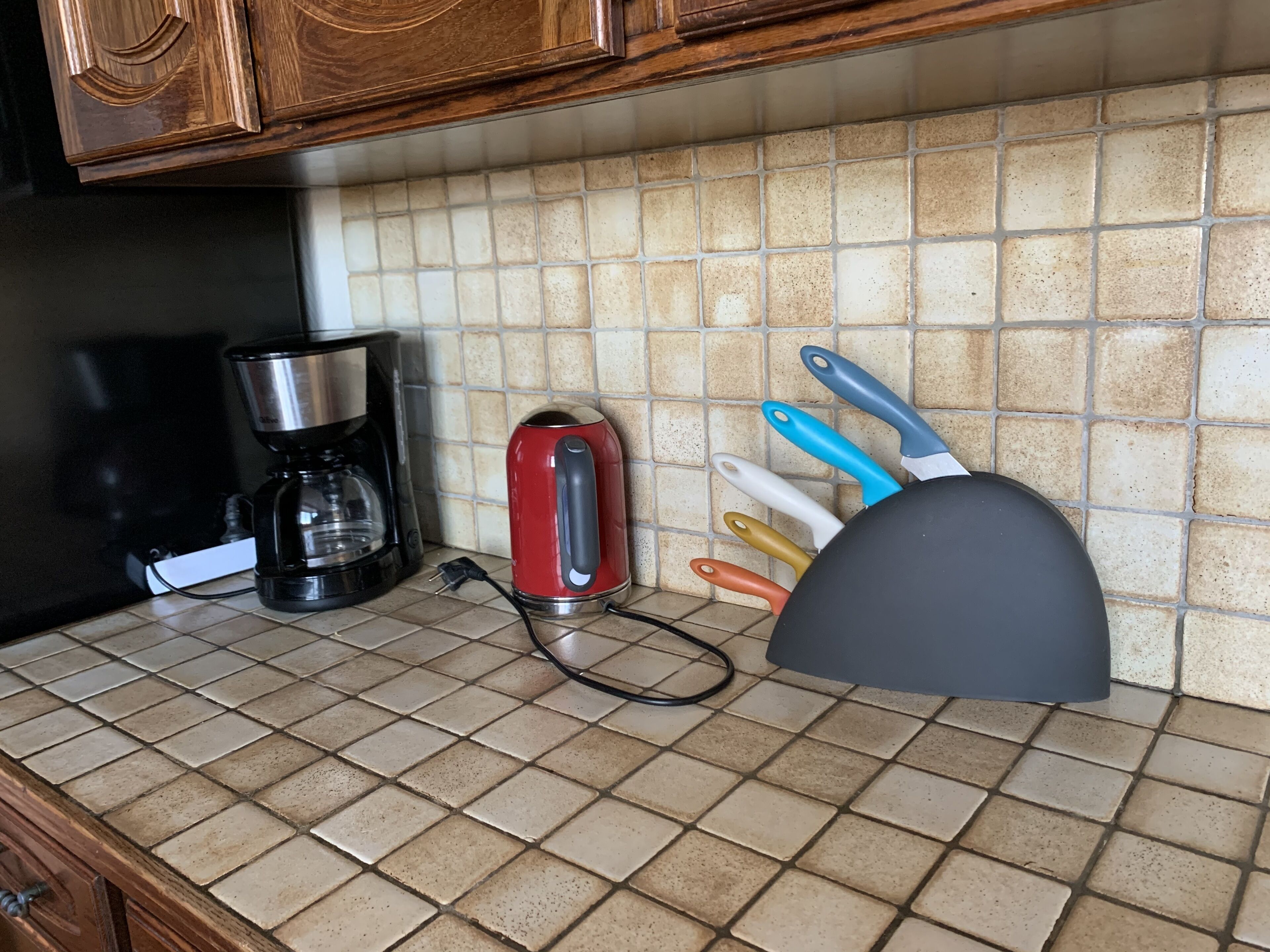 A kitchen counter with a coffee maker, a red kettle, and a set of colorful kitchen utensils.