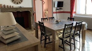 A dining area with a wooden table, chairs, a clock, a television, and a fireplace.