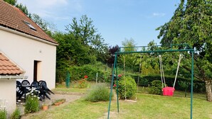 A garden with a swing set, a small building with outdoor seating, and a lawn.