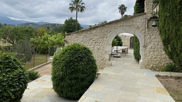 Un arc en pierre mène à un patio aménagé avec du mobilier d’extérieur.