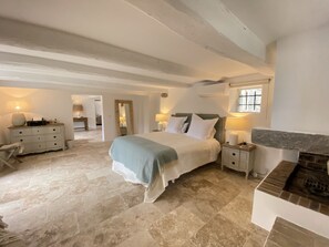 Ein Schlafzimmer mit einem großen Bett, Nachttischen, einer Kommode und einem Kamin aus Stein.