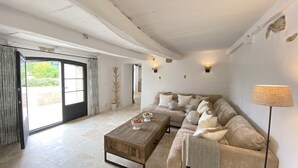 Un salon spacieux avec un grand canapé, une table basse et une lampe. Une porte donne accès à un balcon.