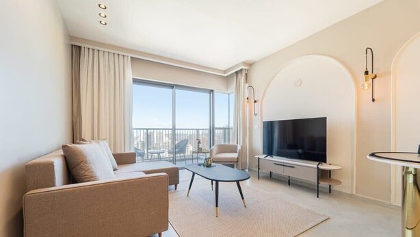 A modern living room with a sofa, a coffee table, a TV, and a balcony with a view.