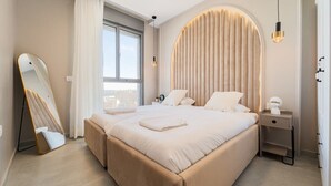 A modern bedroom with a large bed, a bedside table, a mirror, and a window with curtains.