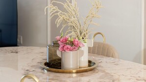 A dining area with a marble table, a vase with flowers, and a modern pendant light.