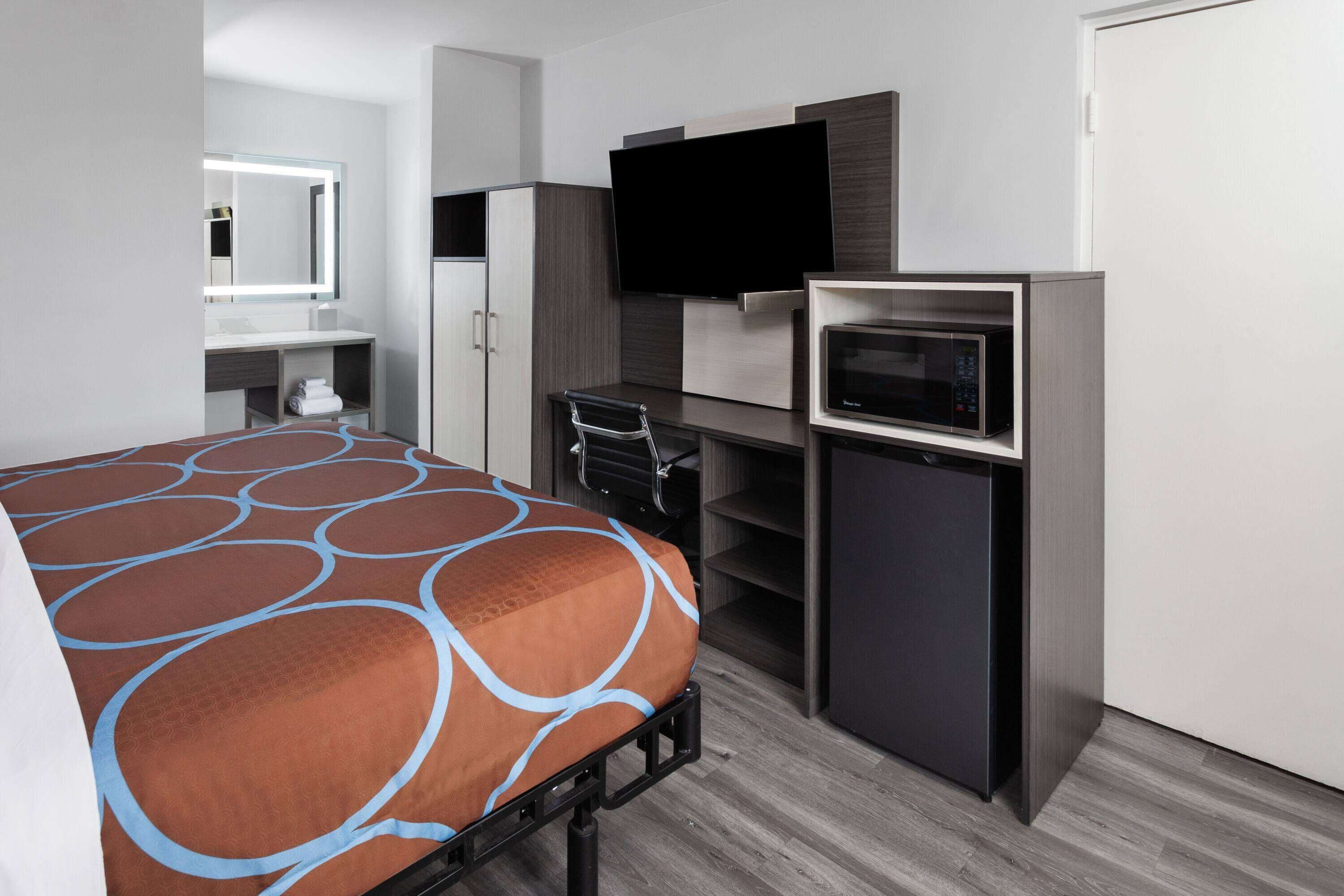 Habitación de hotel con cama, escritorio, televisor de pantalla plana, microondas y armario.